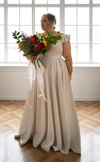 Plus-size bride holding a bouquet, representing Ashley Stewart’s bridal collection launch executed by BrandLoom